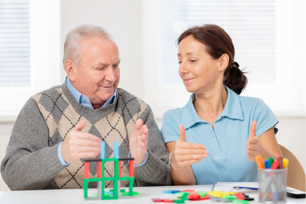 A caregiver gesturing with an older man white arranging blocks.